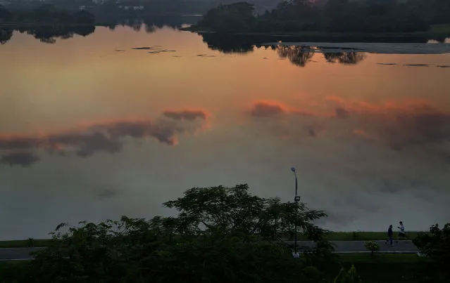 Men walk in a lane adjoining Inye lake, mirrored with colorful-clouds as the sun sets in Yangon, Myanmar, Thursday, December 4, 2014. (Photo by Gemunu Amarasinghe/AP Photo)