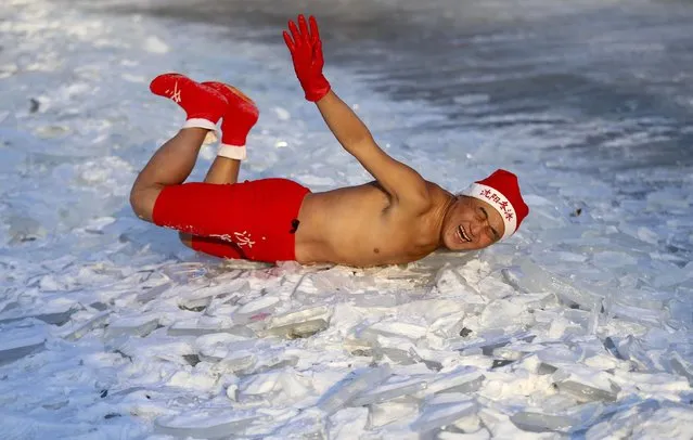 A winter swimmer, wearing a Santa Claus hat to celebrate the upcoming Christmas, reacts as he plays on a frozen lake at a park in Shenyang, Liaoning province, December 22, 2014. The characters on the hat read: “Shenyang Winter Swimming”. (Photo by Reuters/Stringer)