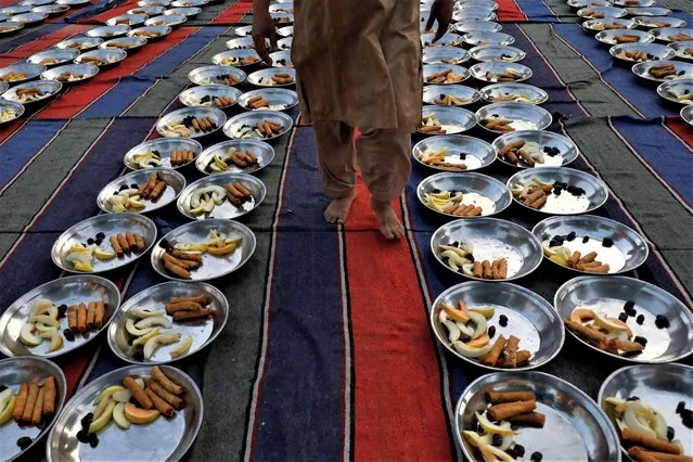 A man walks to inspect food plates before Iftar (breaking fast) during the fasting month of Ramadan, in Karachi, Pakistan on March 23, 2023. (Photo by Akhtar Soomro/Reuters)