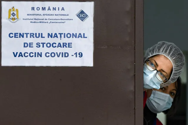Medical staff wearing masks for protection against the COVID-19 infection peer from behind a door at the the National Center for Storage of the COVID-19 Vaccine, a military run facility, in Bucharest, Romania, Friday, December 18, 2020. Romanian authorities plan to start COVID-19 vaccinations on Dec. 27, 2020. (Photo by Andreea Alexandru/AP Photo)
