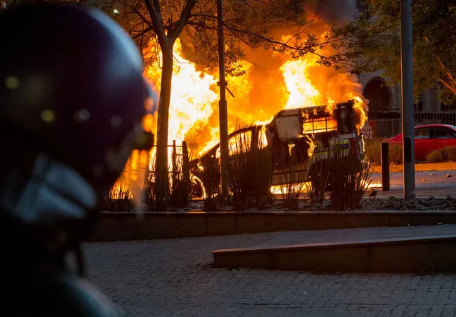 A riot policeman watches as a police vehicle burns in Braamfontein, Johannesburg, South Africa, Tuesday, October 25, 2016. Rioters in South Africa set a police vehicle on fire Tuesday and stoned vehicles near a Johannesburg university that has been the scene of sometimes violent protests by students demanding free education. The violence broke out in streets near the University of the Witwatersrand at around the same time that student protesters met and marched off the campus, South African media reported. (Photo by Yeshiel Panchia/AP Photo)