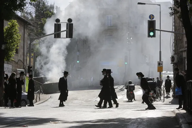 Men walk amid smoke from a dumpster fire, in an ultra-Orthodox neighborhood in Jerusalem, Sunday, January 24, 2021. Ultra-Orthodox demonstrators clashed with Israeli police officers dispatched to close schools in Jerusalem and Ashdod that had opened in violation of health regulations on Sunday. (Photo by Sebastian Scheiner/AP Photo)