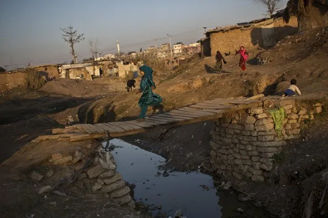 An Afghan refugee girl runs on a wooden bridge over a stream of rain water and sewage in a slum on the outskirts of Islamabad, Pakistan, Saturday, January 17, 2015. (Photo by Muhammed Muheisen/AP Photo)