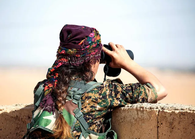 Shirin, 25, a member of the Kurdish female Women' s Protection Units (YPJ) views the battlefield with binoculars from atop a house in the Syrian village of Mazraat Khaled, some 40 kms away from the Islamic State group' s (IS) de- facto capital of Raqa on November 9, 2016 The YPJ are female brigades fighting alongside male fighters of the Syrian Democratic Forces (SDF), the militia alliance supported by the United States in the offensive launched on November 5 to capture Raqa from IS jihadists. (Photo by Delil Souleiman/AFP Photo)