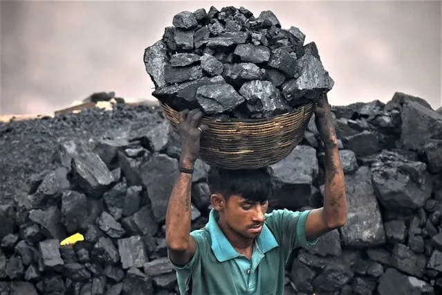A coal picker carries coal from near an open cast mining site on the outskirts of Dhanbad on July 6, 2023. (Photo by Money Sharma/AFP Photo)