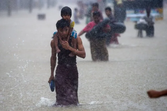 A man carries a child through floodwaters in the Bago region, some 68 km away from Yangon, on July 29, 2018. Heavy monsoon rains have pounded Karen state, Mon state and Bago region in recent days and show no sign of abating, raising fears that the worst might be yet to come. (Photo by Ye Aung/AFP Photo)