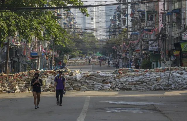 People walk along a deserted road blocked with improvised barricades build by anti-coup protesters to secure a neighborhood in Yangon, Myanmar, Thursday, March 18, 2021. (Photo by AP Photo/Stringer)