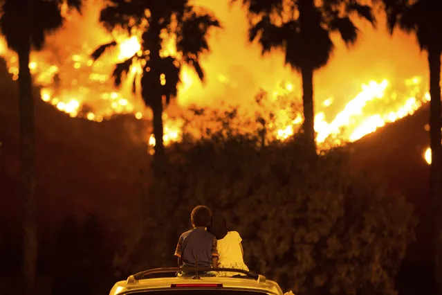 King Bass, 6, left, sits and watches the Holy Fire burn from on top of his parents' car as his sister Princess, 5, rests her head on his shoulder Thursday night, August 9, 2018 in Lake Elsinore, Calif. More than a thousand firefighters battled to keep a raging Southern California forest fire from reaching foothill neighborhoods Friday before the expected return of blustery winds that drove the flames to new ferocity a day earlier. (Photo by Patrick Record/AP Photo)