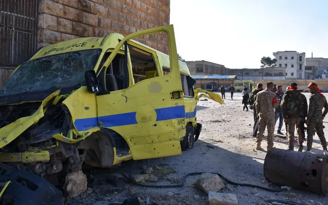 Syrian pro-government forces stand next to the wreckage of an ambulance outside a makeshift hospital which was used by rebel fighters in Aleppo's al-Sakhur neighbourhood, on December 6, 2016, a few days after the area was retaken by the government troops. (Photo by George Ourfalian/AFP Photo)