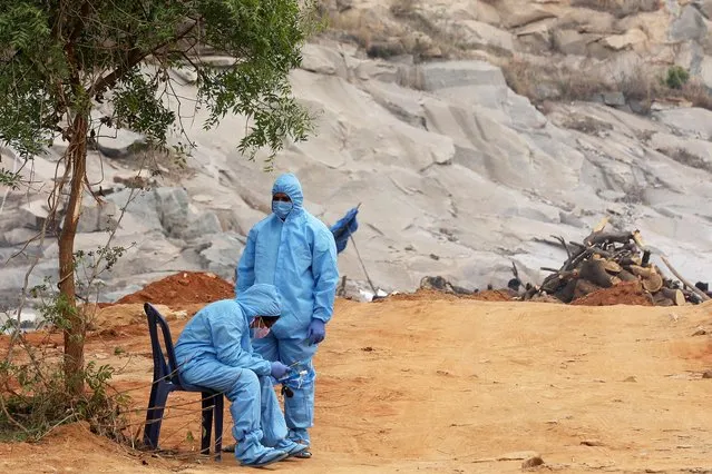 Relatives wear Personal Protective Equipment (PPE) as they wait to cremate their loved ones at a mass cremation ground in Giddenahalli on the outskirts of Bangalore, India, 03 May 2021. India recorded a massive surge of 357,229 fresh COVID-19 cases and 3,449 deaths in the last 24 hours. (Photo by Jagadeesh N.V./EPA/EFE)