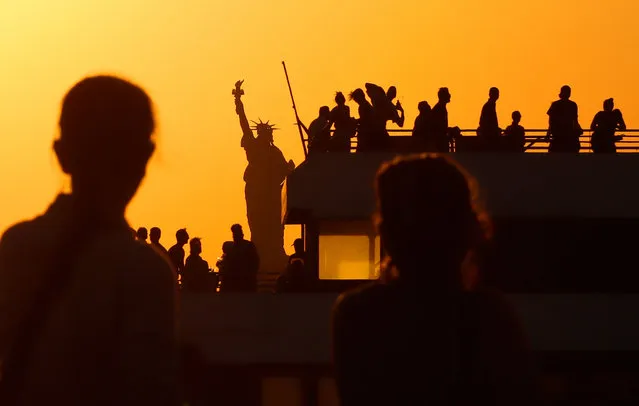 People watch the sun set behind the Statue of Liberty from a pier in Brooklyn as a ferry passes by on June 5, 2021 in New York City. (Photo by Gary Hershorn/Getty Images)