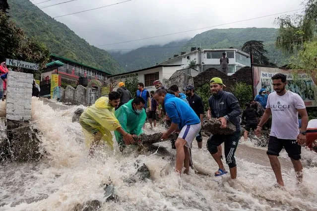People place rocks to divert sudden gush of water during flash floods after heavy monsoon rains in Bhagsunag, a popular tourist town in Himachal Pradesh, India, Monday, July 12, 2021. (Photo by Ashwini Bhatia/AP Photo)