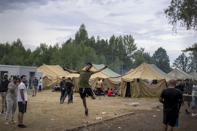 A migrant jumps as other walk inside the newly built refugee camp in the Rudninkai military training ground, some 38km (23,6 miles) south from Vilnius, Lithuania, Wednesday, August 4, 2021. The Red Cross warned Wednesday that Lithuania's decision to turn away immigrants attempting to cross in from neighboring Belarus does not comply with international law. Lithuania, a member of the European Union, has faced a surge of mostly Iraqi migrants in the past few months. Some 4,090 migrants, most of them from Iraq, have crossed this year from Belarus into Lithuania. (Photo by Mindaugas Kulbis/AP Photo)