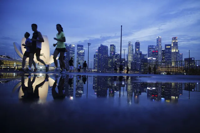 Joggers run pass as the skyline of Singapore's financial district is seen in the background April 21, 2014. (Photo by Edgar Su/Reuters)