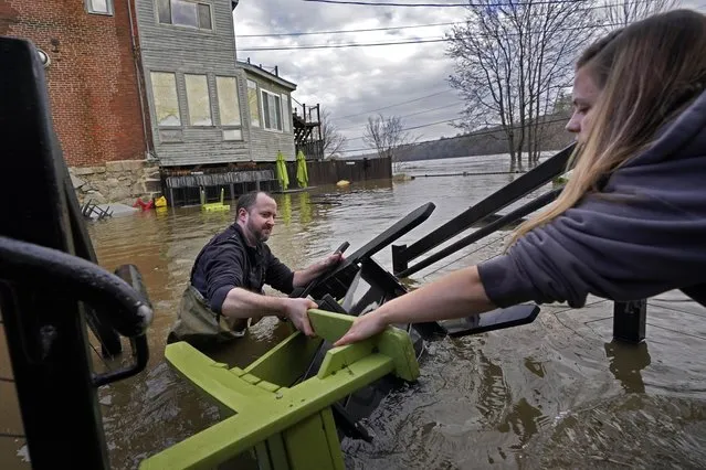 Nathan Sennett hands furniture to Tori Grasse as they work in hip-deep water on the patio of the Quarry Tap Room, Tuesday, December 19, 2023, in Hallowell, Maine. Waters continue to rise in the Kennebec River following Monday's severe storm. (Photo by Robert F. Bukaty/AP Photo)