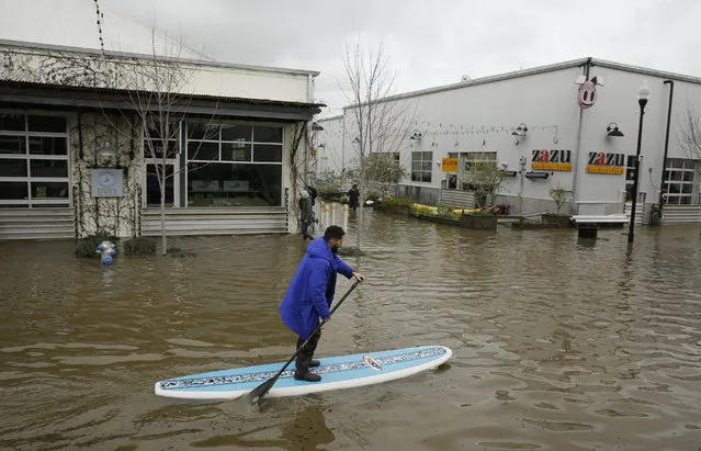 A man uses a paddle board to make his way through the flooded Barlow Market District Wednesday, February 27, 2019, in Sebastopol, Calif. (Photo by Eric Risberg/AP Photo)