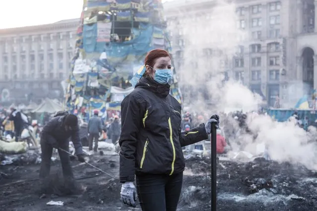A woman clears ashes and debris with other anti-government protesters from a newly-occupied portion of Independence Square on February 20, 2014 in Kiev, Ukraine. (Photo by Brendan Hoffman/Getty Images)