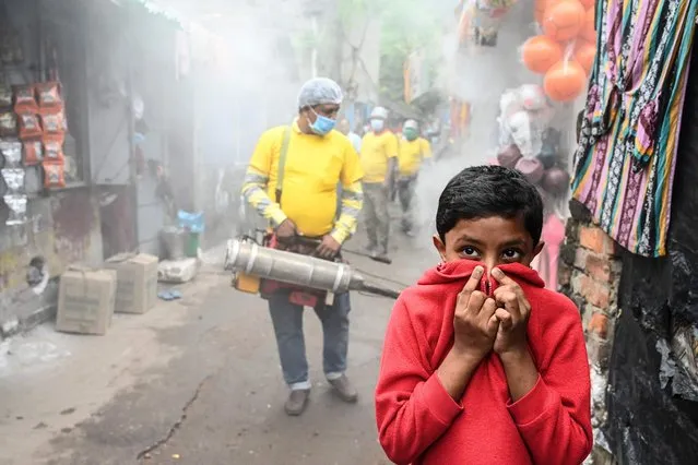 A child covers his face while a municipal worker fumigates a slum area as a preventive measure against mosquito-born diseases in Kolkata on November 15, 2021. (Photo by Dibyangshu Sarkar/AFP Photo)