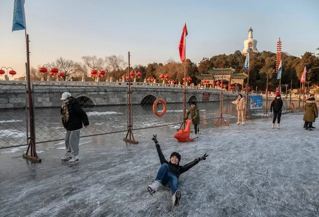 A woman reacts as she lays on the ice to have her photo taken by a friend while skating on an outdoor rink at Beihai Lake on January 11, 2022 in Beijing, China. (Photo by Kevin Frayer/Getty Images)