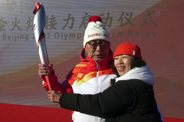 First Torch bearer Luo Zhihuan and his wife poses with the torch at the start of the torch relay for the 2022 Winter Olympics at the Olympic Forest Park in Beijing on Wednesday, February 2, 2022. (Photo by Sam McNeil/AP Photo)