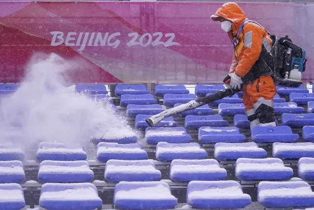 A worker clears snow from the seats in the finish area at the alpine ski venue at the 2022 Winter Olympics, Sunday, February 13, 2022, in the Yanqing district of Beijing. (Photo by Robert F. Bukaty/AP Photo)