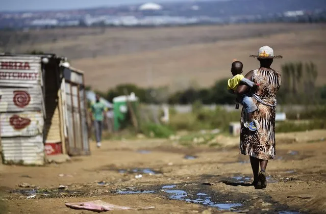 A woman carries her child as she walks alongside a line of shacks in the impoverished township of Diepsloot on the outskirts of Centurion on April 24, 2014. South Africans will mark 20 years of democracy since the first post-Apartheid election on April 27, 1994. (Photo by Mujahid Safodien/AFP Photo)