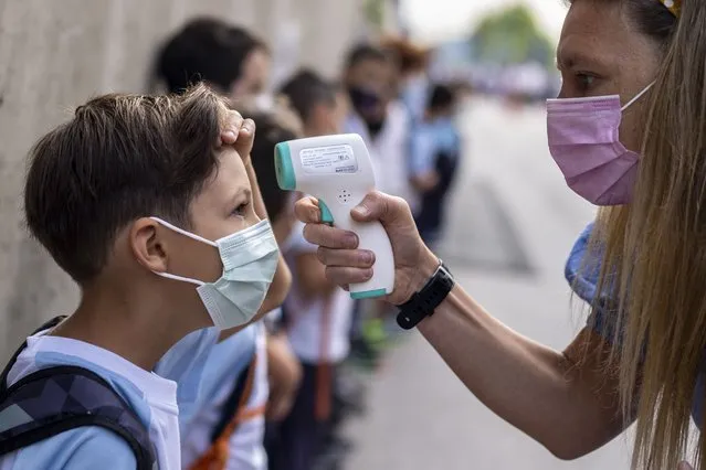 A teacher wearing a face mask to protect against the spread of coronavirus checks the temperature of her student at Maestro Padilla school as the new school year begins, in Madrid, September 7, 2021. With one of Europe's highest vaccination rates and its most pandemic-battered economies, the Spanish government is laying the groundwork to approach the virus in much the same way countries deal with flu or measles. (Photo by Manu Fernandez/AP Photo/File)