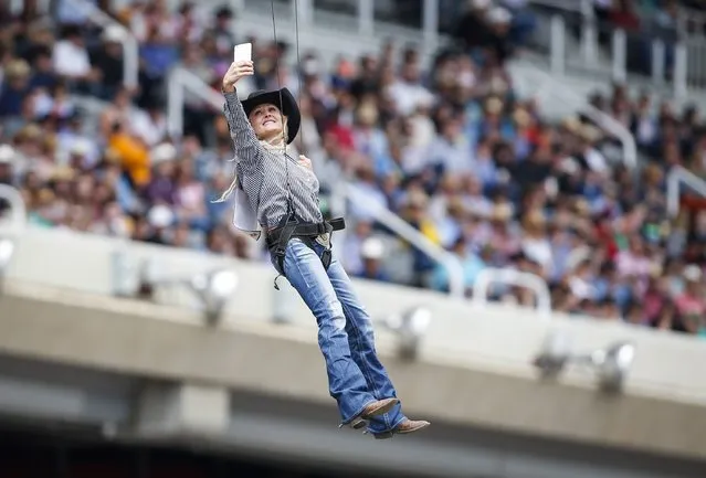 Barrel racer Carlee Pierce of Marietta, Okla., takes a photo as she is lowered on wires into the Calgary Stampede rodeo grounds during opening ceremonies in Calgary, Alberta, Sunday, July 5, 2015. (Photo by Jeff McIntosh/The Canadian Press via AP Photo)