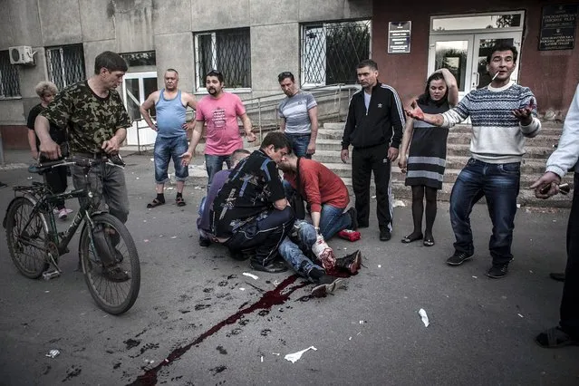 Local residents watch as others give first aid to a man who was shot in the leg by Ukranian militia in the village of Krasnoarmisk, Ukraine, 11 May 2014. Eyewitness said that Ukranian militia tried to stop the referendum voters briefly taking the City Hall of Krasnoarmisk, where unarmed pro-Russian supporters were gathering. (Photo by EPA/Maysun)