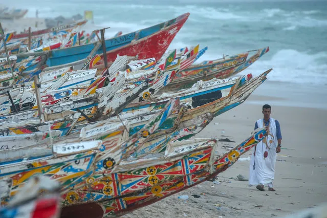 A fisherman walks past wooden fishing boats stacked on the shore in Nouakchott, Mauritania on August 11, 2019. Fishing is one of the most important sources of income in Mauritania, a West African country with 754 kilometers of coastline to the Atlantic Ocean. Hundreds of fishermen who come to the shores of the capital Nouakchott early with the daylights go for fishing in the ocean with their colorful boats. Fishermen struggle until the dusk to make a living out of fishing by selling them at a market by the ocean. (Photo by Ozkan Bilgin/Anadolu Agency via Getty Images)