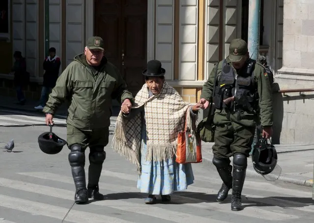 Riot police officers help an elderly woman at Murillo square during a protest by Potosi miners (not pictured) in La Paz, Bolivia July 21, 2015. (Photo by David Mercado/Reuters)