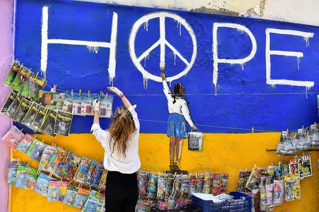 A newsagent picks up magazines next to a mural by Italian urban artist Salvatore Benintende aka “TV BOY” depicting a girl painting a peace symbol on an Ukraine's flag, reading “Hope” in Barcelona on April 30, 2022. (Photo by Pau Barrena/AFP Photo)