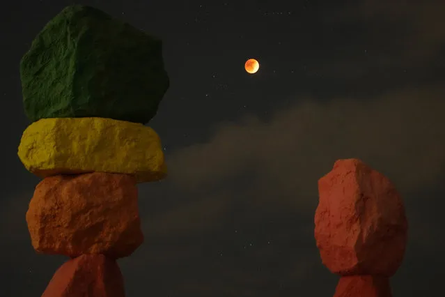 A lunar eclipse is seen above the artwork titled: “Seven Magic Mountains” by artist Ugo Rondinone, during the first blood moon of the year Sunday, May 15, 2022, near Jean, Nev. (Photo by John Locher/AP Photo)
