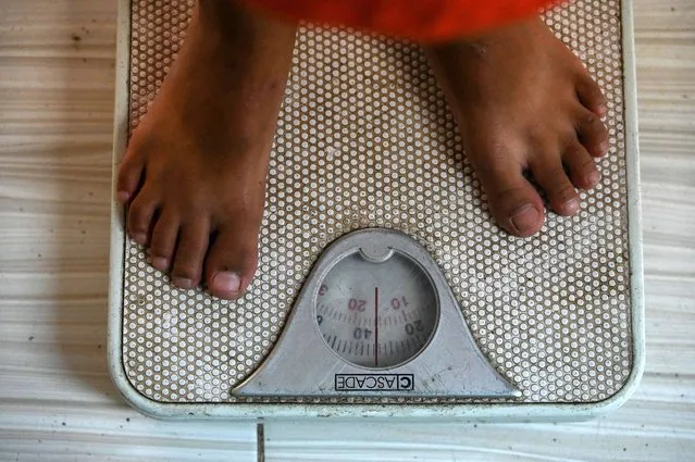 In this photo taken on June 26, 2022, an elementary student, a beneficiary of the Department of Education's meals programme for undernourished children, is weighed on a scale in Bulacan, north of Manila. (Photo by Jam Sta Rosa/AFP Photo)