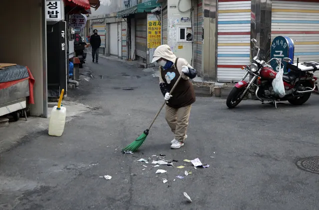 A woman wearing a face mask sweeps on the street in the morning in Seoul, South Korea, Wednesday, March 18, 2020. For most people, the new coronavirus causes only mild or moderate symptoms. For some it can cause more severe illness. (Photo by Lee Jin-man/AP Photo)