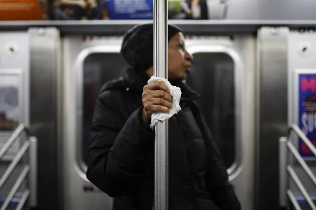 A subway customer uses a tissue to protect her hand while holding onto a pole as COVID-19 concerns drive down ridership, Thursday, March 19, 2020, in New York. Gov. Andrew Cuomo tightened work-from-home rules Thursday as confirmed cases continued to climb in New York, an expected jump as testing becomes more widespread. But he stressed that roadblocks and martial law for New York City were merely rumors. (Photo by John Minchillo/AP Photo)