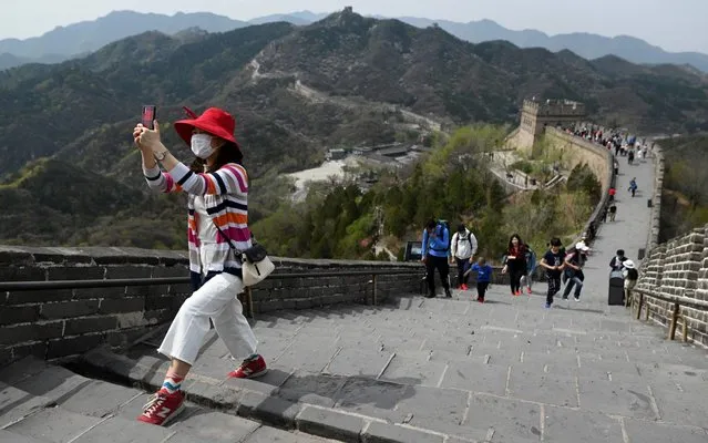 A visitor, wearing a face mask amid concerns of the COVID-19 coronavirus, uses her mobile phone to take a picture as she climbs a steep section of the Great Wall of China in Beijing on April 18, 2020. (Photo by Wang Zhao/AFP Photo)