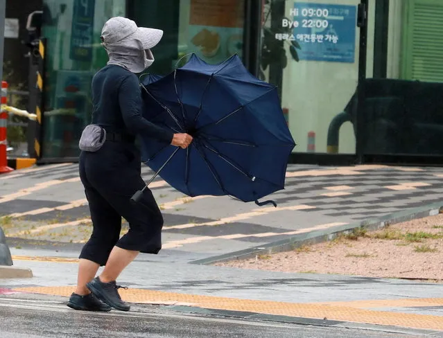 A woman struggles to hold onto her umbrella in strong winds brought by the powerful Typhoon Nanmadol near a port in Busan, South Korea, 19 September 2022, as the powerful Typhoon Nanmadol, the 14th this season, is projected to hit the country's southeastern part later in the day. (Photo by Yonhap/EPA/EFE)