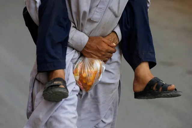 A laborer carries his son on his back while holding a charity food handout as they head home during a lockdown in Karachi, Pakistan on May 6, 2020. (Photo by Akhtar Soomro/Reuters)