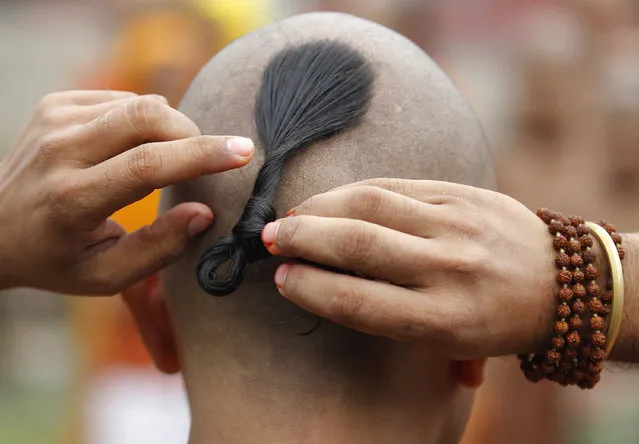 A Nepalese Hindu priest adjusts his hair while performing rituals during Janai Purnima festival in Kathmandu, Nepal, Thursday, August 18, 2016. During this festival Hindus take holy baths and perform annual change of the Janai, a sacred cotton string worn around their chest or tied on the wrist, in the belief that it will protect and purify them. (Photo by Niranjan Shrestha/AP Photo)