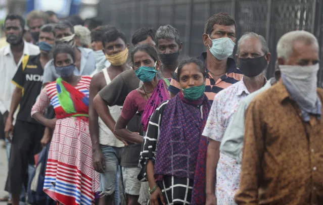 Homeless people wearing masks stand in a queue to receive food being distributed in Mumbai, India, Saturday, June 20, 2020. India is the fourth hardest-hit country by the COVID-19 pandemic in the world after the U.S., Russia and Brazil. (Photo by Rafiq Maqbool/AP Photo)