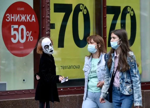 A clothing store promoter wearing a theatrical mask gives out advertising leaflets to passers-by wearing face masks in the center of the Ukrainian capital of Kiev on July 15, 2020. (Photo by Sergei Supinsky/AFP Photo)