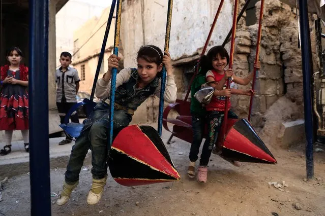 Syrian children play on swings, made from the remnants of exploded rockets in the rebel-held town of Douma, on the eastern edges of the capital Damascus, on September 14, 2016, on the third day of Eid al-Adha Muslim holiday. Syrian children love playgrounds like kids all over the world but in rebel-held towns near Damascus swing sets are made of spent rockets and jungle gyms are tucked underground. (Photo by Sameer Al-Doumy/AFP Photo)
