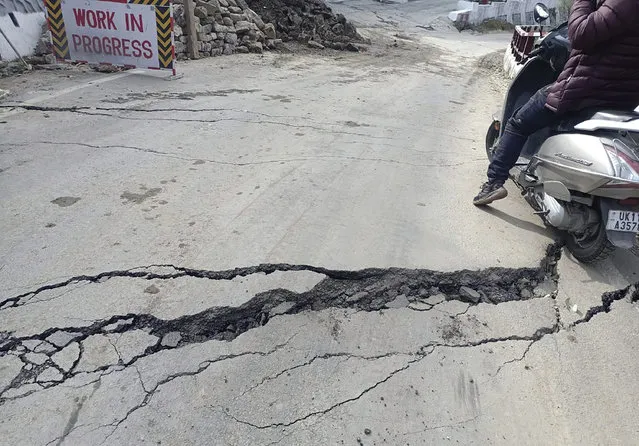 A motorist navigates his way through a crack on a road in Joshimath, India, Tuesday, January 3, 2023. Authorities have stopped all construction activity and started shifting hundreds of people panicking after seeing a temple collapse and cracks in over 600 houses due to subsidence of land in a northern Indian hilly town, officials said on Saturday. (Photo by AP Photo/Stringer)