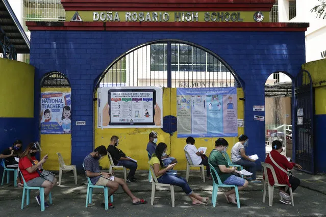 People wearing masks and face shields wait for their turn to pick up student electronic tablets as online classes are scheduled to start next week in the Dona Rosario High School in Quezon city, Philippines, Thursday, October 1, 2020. Public schools will hold online classes using electronic gadgets and educational materials provided to students as the opening got delayed due to the coronavirus pandemic. (Photo by Aaron Favila/AP Photo)