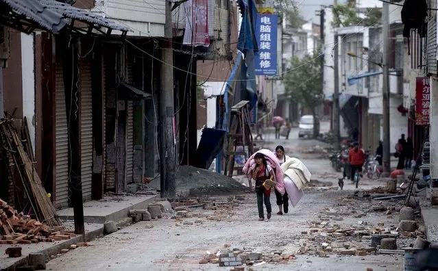 People carrying their belongings through the quake-damaged Gucheng Village in Lushan County in China's Sichuan Province, on April 20, 2013. (Photo by Fei Maohua/Xinhua)