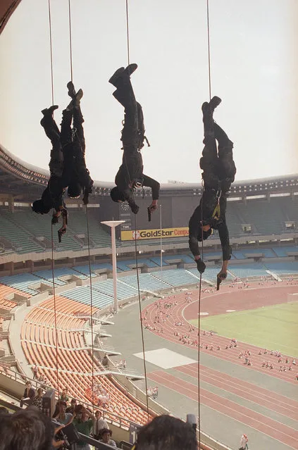 South Korean antiterrorist commandos slide down ropes with guns drawn during a training exercise in the main Olympic Stadium in Seoul, June 17, 1988. (Photo by Tsugufumi Matsumoto/AP Photo)