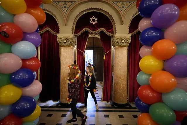 Children wearing colourful flower necklaces enter the Coral Temple synagogue as Romania's Jewish community celebrates Purim in Bucharest, Romania, Monday, March 6, 2023. The Jewish holiday of Purim commemorates the Jews' salvation from genocide in ancient Persia, as recounted in the Book of Esther. (Photo by Andreea Alexandru/AP Photo)