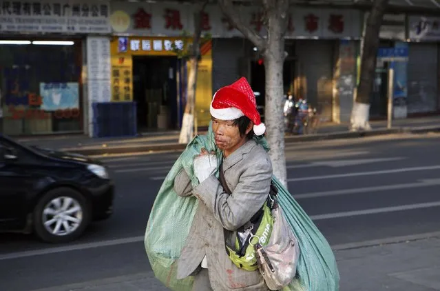 A man wearing a Santa hat carries giant bags as he walks along a street at an old area of Liwan district in Guangzhou, Guangdong province December 23, 2014. (Photo by Alex Lee/Reuters)