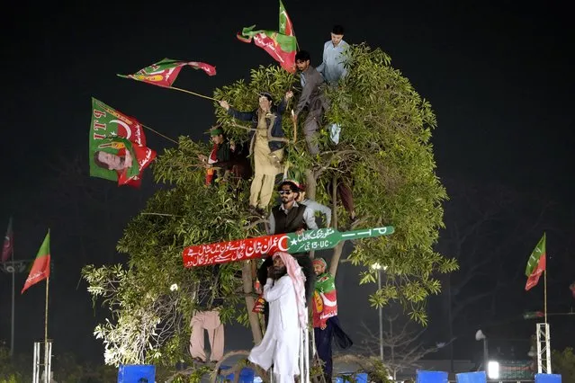Standing in a tree, supporters of former Prime Minister Imran Khan listen to his speech during a rally in Lahore, Pakistan, Sunday, March 26, 2023, to pressure the government of Shahbaz Sharif to agree to hold snap elections. (Photo by K.M. Chaudary/AP Photo)